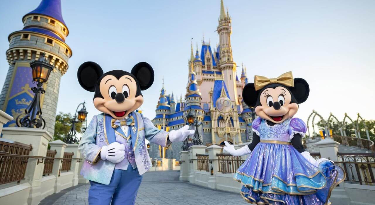 Mickey Mouse and Minnie Mouse in festive, sparkly outfits posing proudly in front of Cinderella Castle at Magic Kingdom, Orlando, highlighting complete Disney travel services.